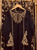 Black dress with gold lace details on a hanger against a decorative curtain background