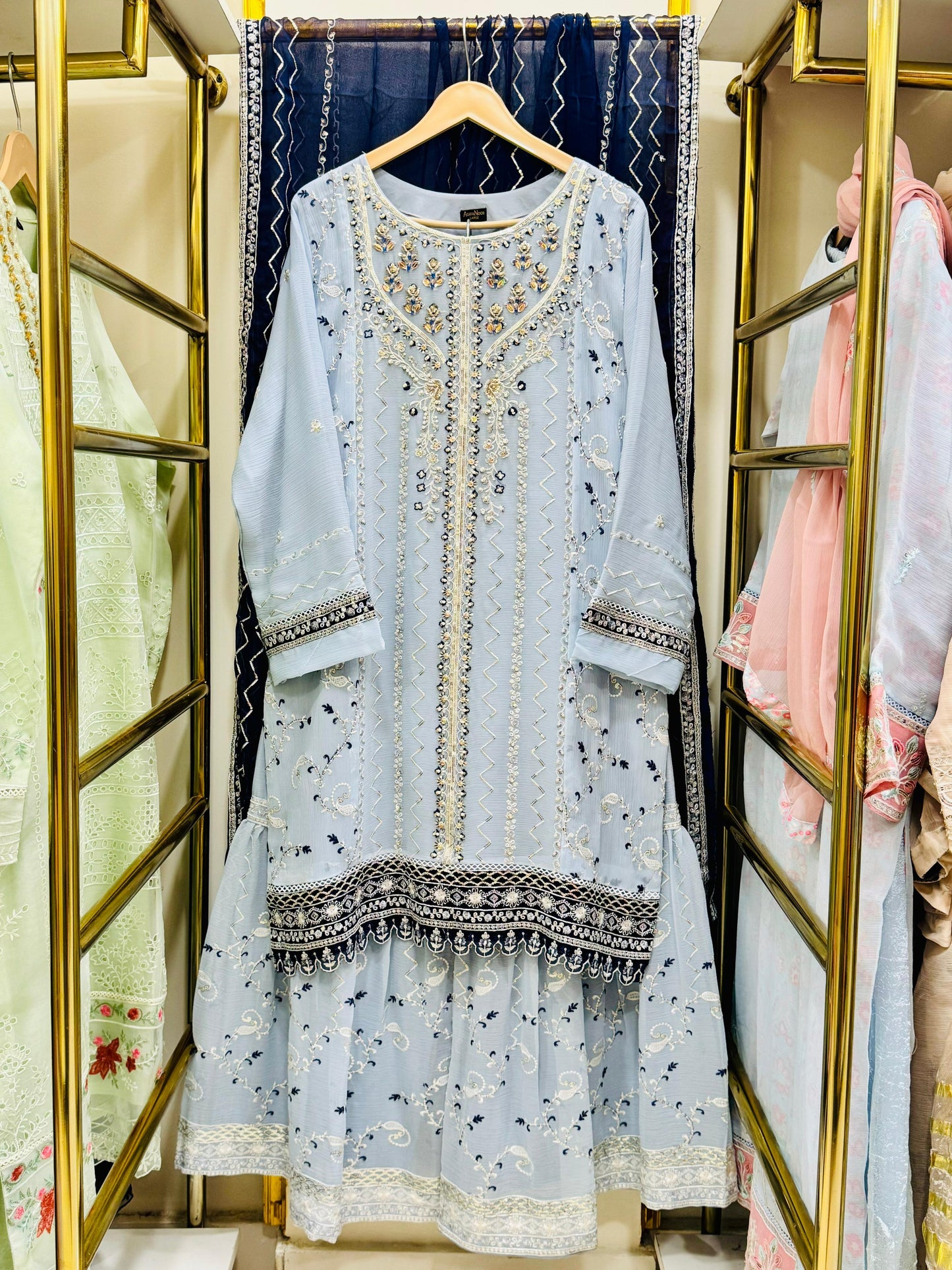 Light blue embroidered  gHARARA dress hanging on a rack with floral patterns in the background