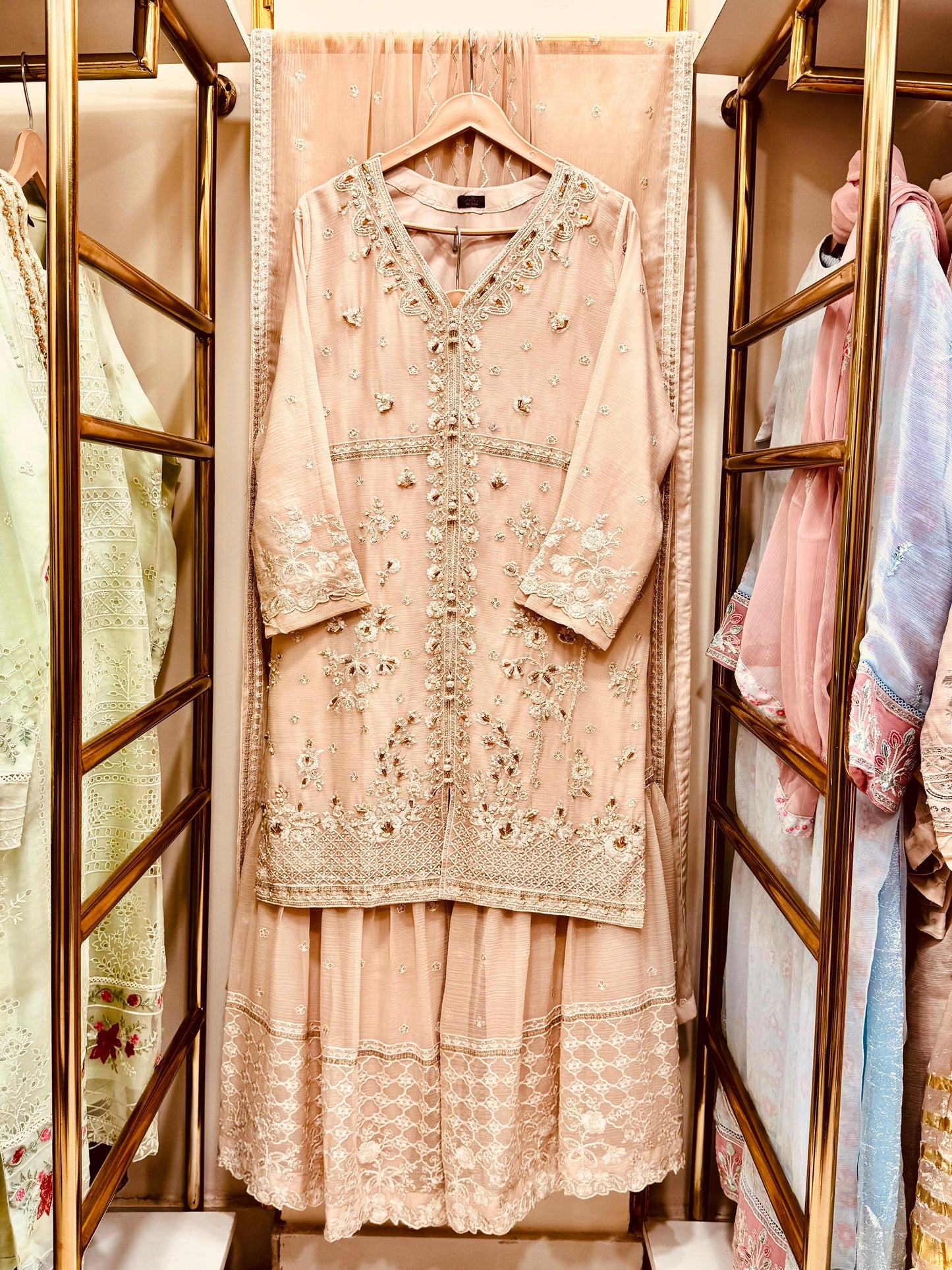 Delicate pink embroidered outfit hanging in a store with a wooden rack.