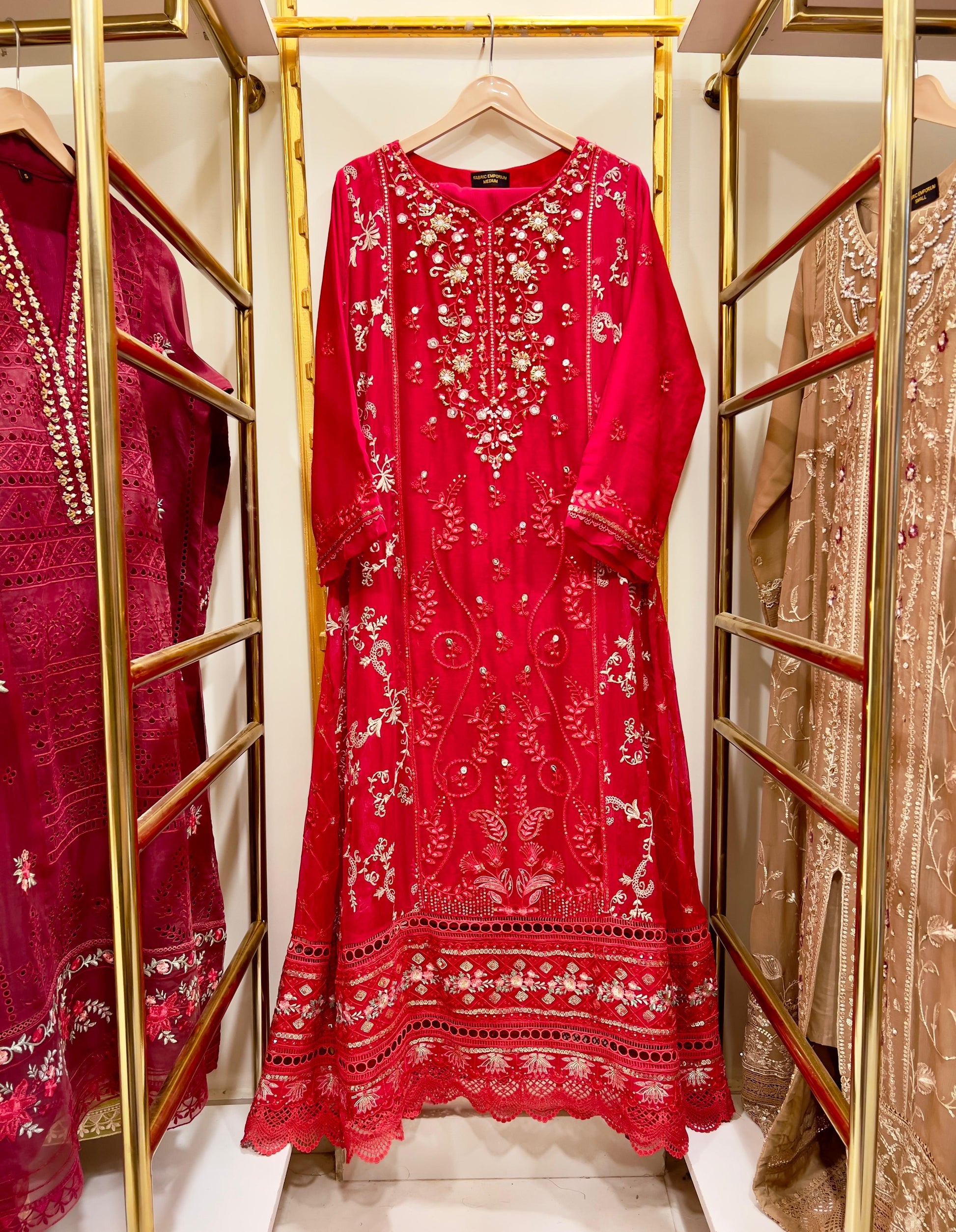 Red embroidered  gown dress on a hanger with gold racks and other dresses in the background